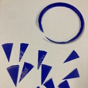 Image corresponding with step two of the instructions to make your own needle. A blue plastic lid has been cut to remove the rounded edge, and the flat part has been cut into small pie piece shapes of roughly the same size.