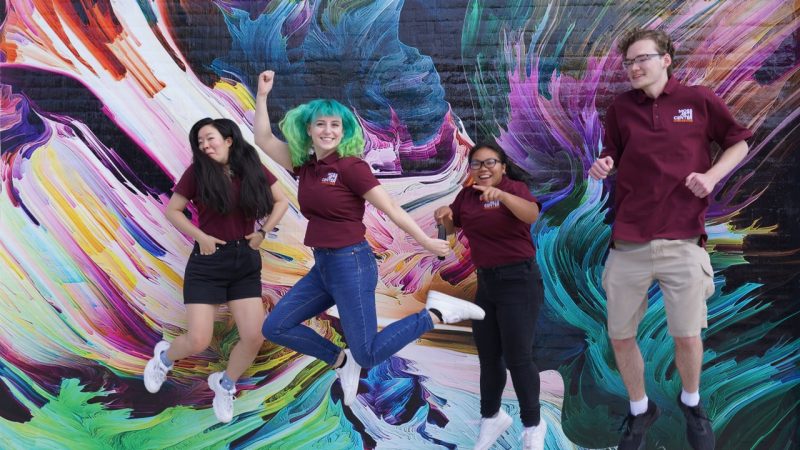  Moss Arts Center Student Ambassadors jump in front of a mural at the Moss Arts Center.