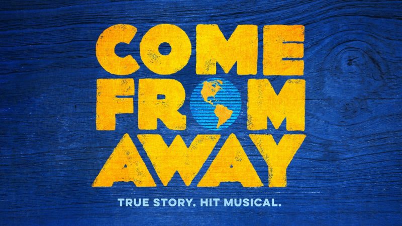  The logo for Broadway show "Come From Away," which is spelled out in yellow text with the O in "From" represented as the earth. Below the title is light blue text that reads "True Story. Hit Musical." The background is a blue woodgrain.
