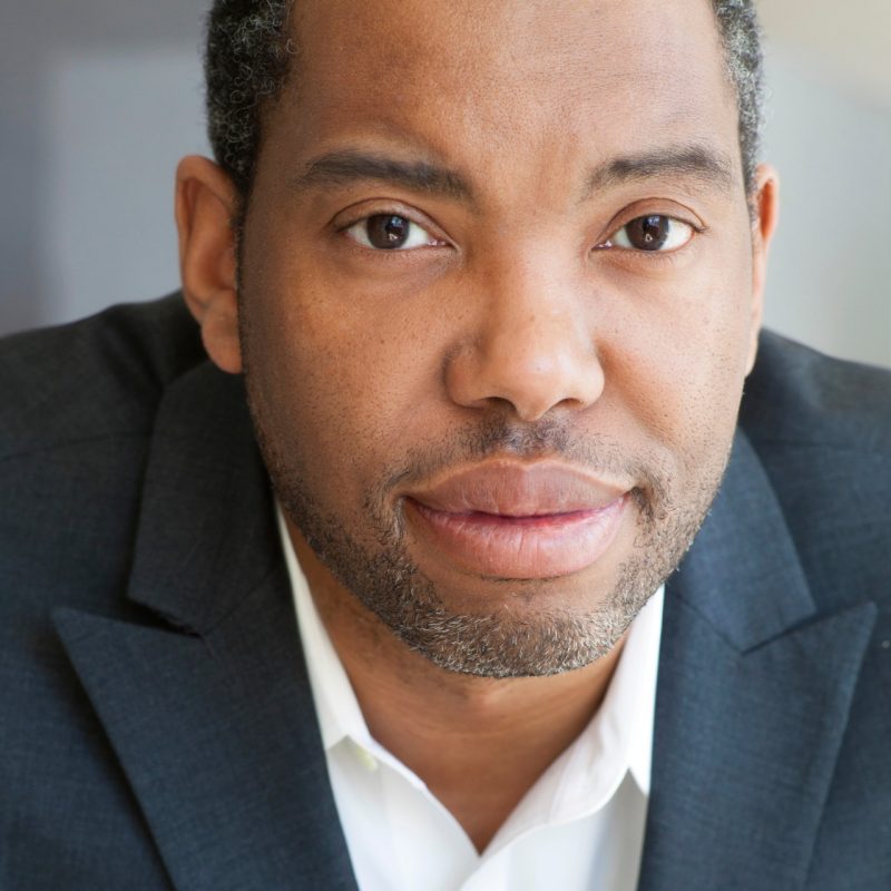 Author Ta-Nehisi Coates, a middle aged Black man with short hair and beard, wears a dark blazer over a light button down shirt in this close up.