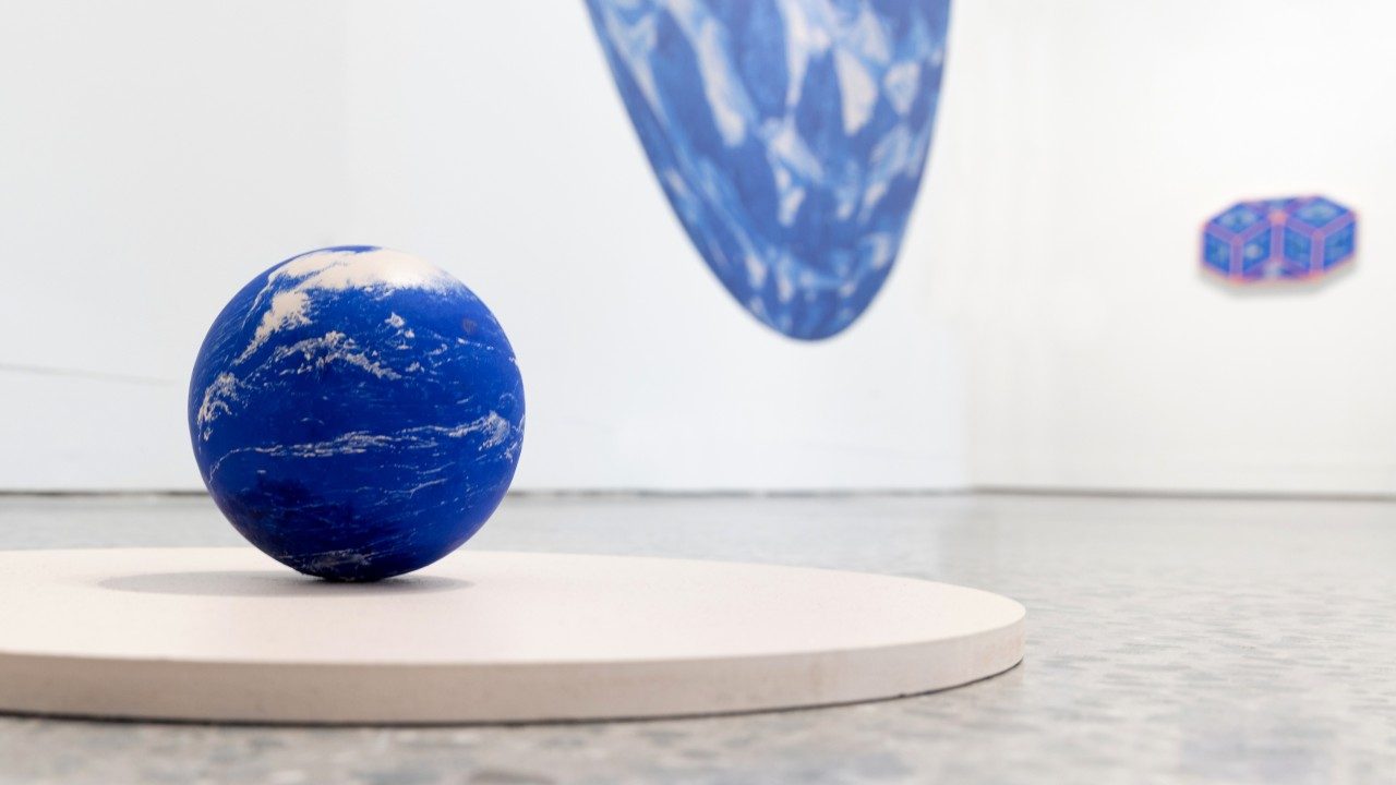  Namwon Choi's "The Shape of Distance" at the Moss Arts Center. A small blue globe that resembles the Earth rests on a flat circular pedestal. Behind it, two other works are visible on white walls.