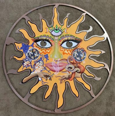 An acrylic painting on a metal cutout by Summer Carlson. The shape is a sun inside a metal circle. A face is painted on the sun with big brown eyes and full eyelashes, multicolored eye shadow, a wide green nose, and full pink lips. On the forehead is a third eye with a green pupil, which seems to be looking up. Two crescent moon shapes flank the third eye. On the right cheek is a red octopus grasping a ball with ying yang koi fish in its tentacles. On the other cheek is another ball with ying yang koi fish and, below that, what sort of looks like rivers flowing to a lake from above. Within the lake section are orangey pink clouds. Near the chin area are two hands resembling Michelangelo's "The Creation of Man," but one hand is holding a smoking blunt.