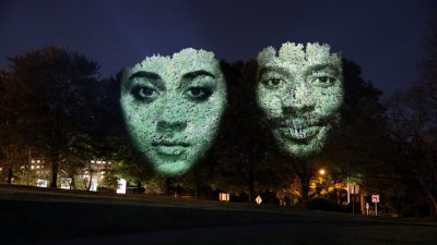  An example of Craig Walsh's "Monuments," enormous night-time projections that transform trees into sculptural monuments. Two faces are projected onto two trees, one woman, left, and a man, right.