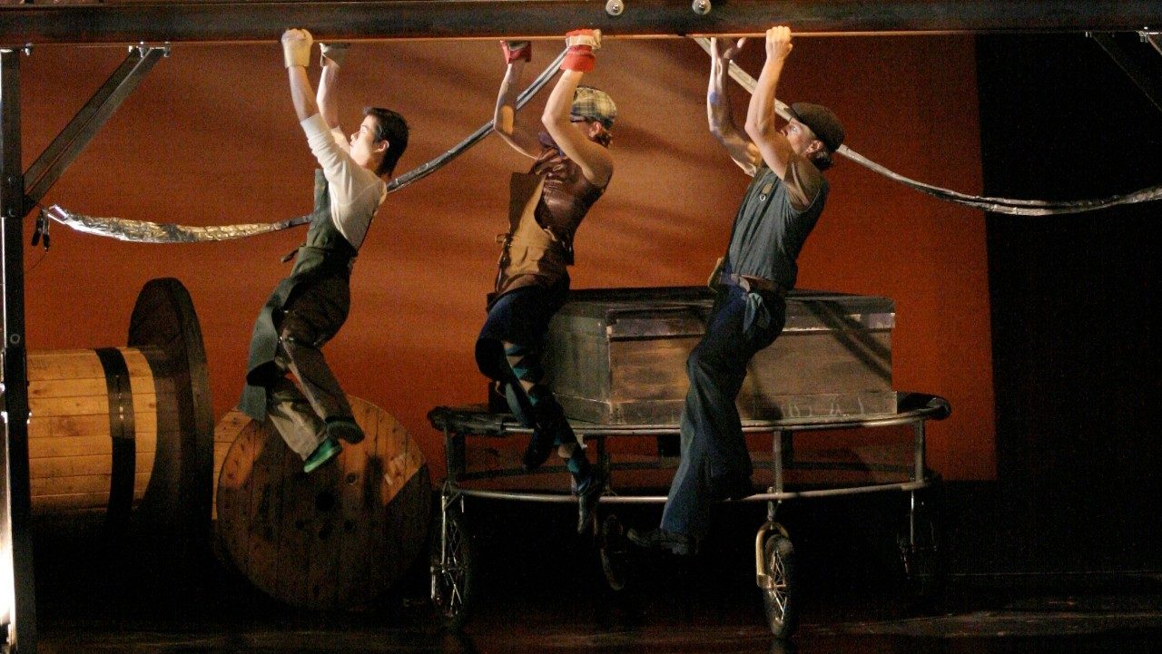  Members of Cirque Mechanics hang from monkey bars on stage.