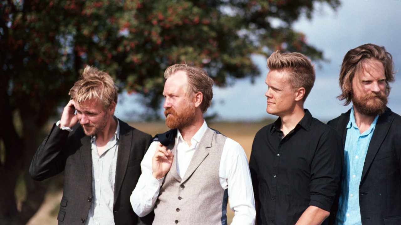  Members of Danish String Quartet stand in a field with a tree in the background wearing button down shirts and jackets