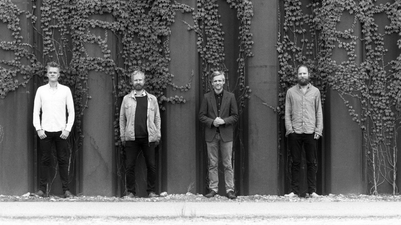  Members of the Danish String Quartet stand in front of an ivy-covered wall, each member framed within an architectural divot. The image is in black and white.