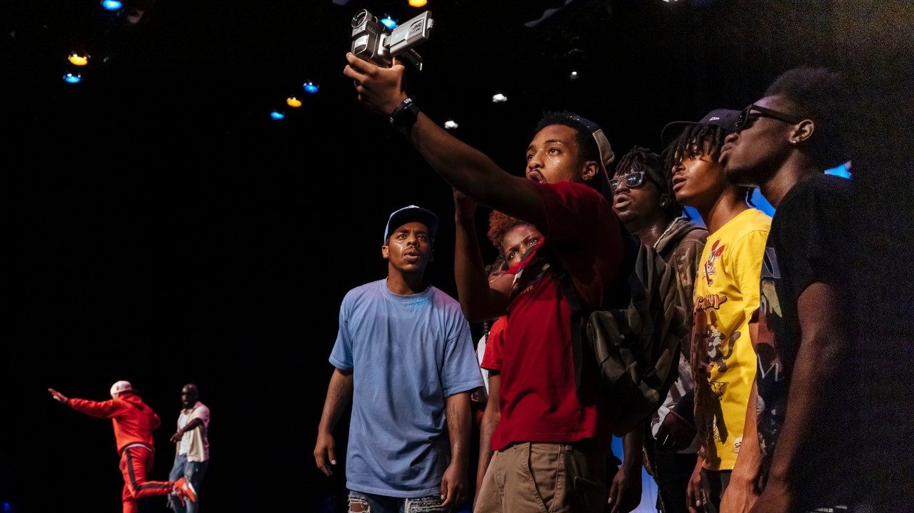  Some of the cast of "Memphis Jookin': The Show" pose together as one man holds a camcorder out in front of him. In the background, two people dance.