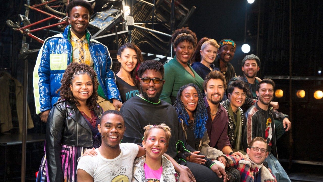  The cast members of "Rent" stand in a group and smile towards the camera