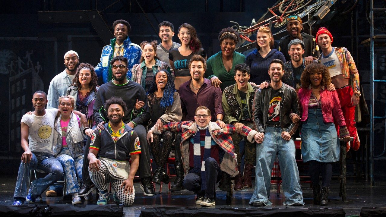  The cast members of "Rent" stand in a group and smile towards the camera