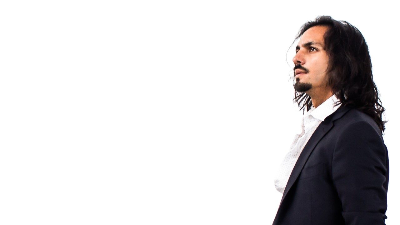  Flamenco dancer Farruquito wears a black suit and a white shirt. He has long dark brown hair and a goatee. He stands in front of a white background and looks off into the middle distance.