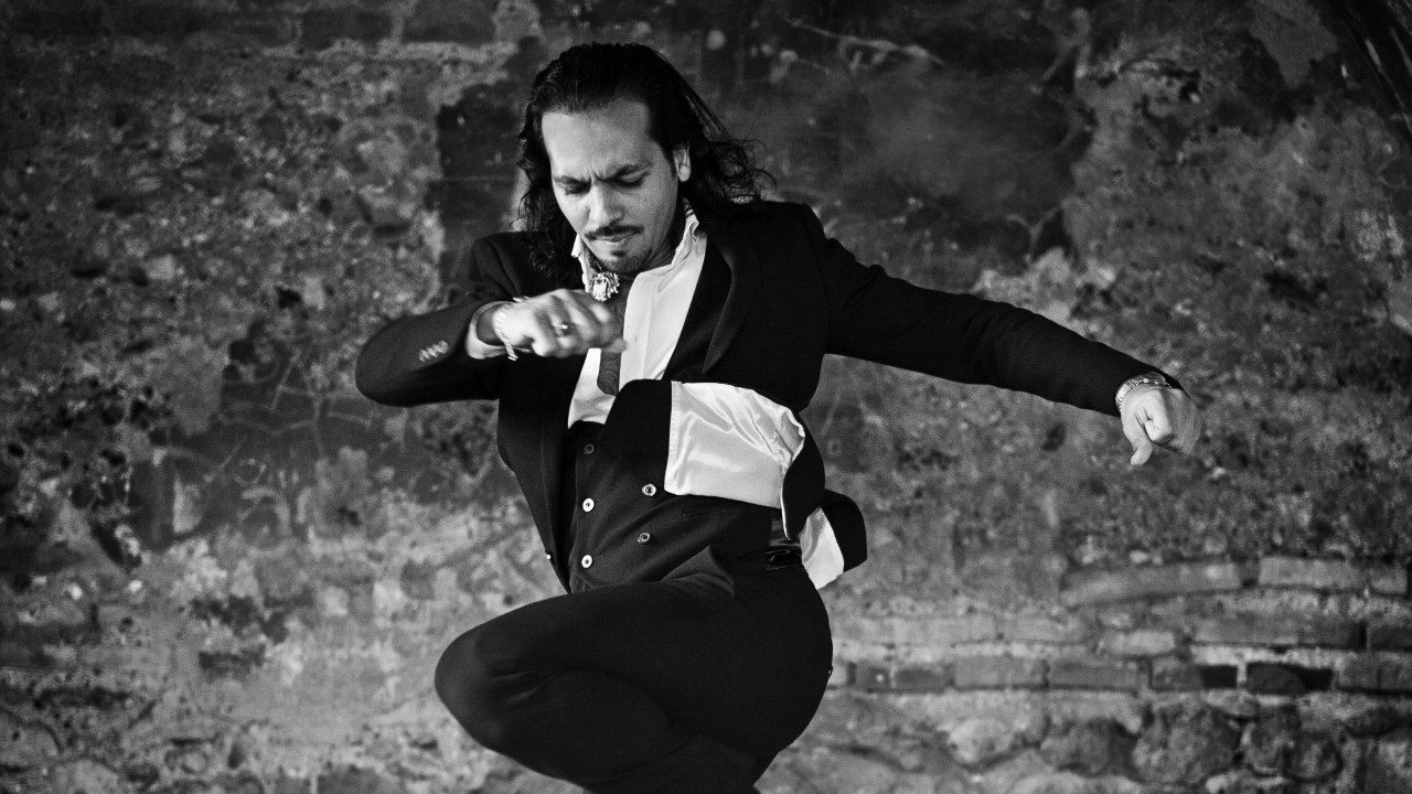  Flamenco dancer Farruquito wears a black and white costume and dances energetically in front of a brick wall in this black and white image.