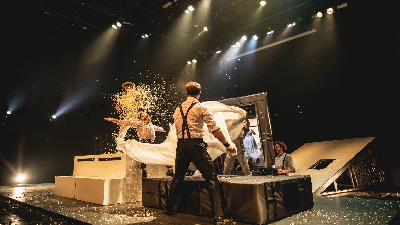  The cast of Machine de Cirque demolish the set, throwing popcorn into the air and snapping a large white sheet. It is chaos.