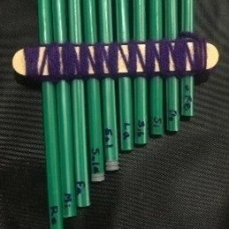 A homemade instrument made from upcycled materials. This pan flute is made from 10 green straws, popsicle sticks, and yarn.