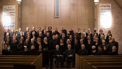  Blacksburg Master Chorale poses for a group photo in a church. The members all wear black and face the camera.