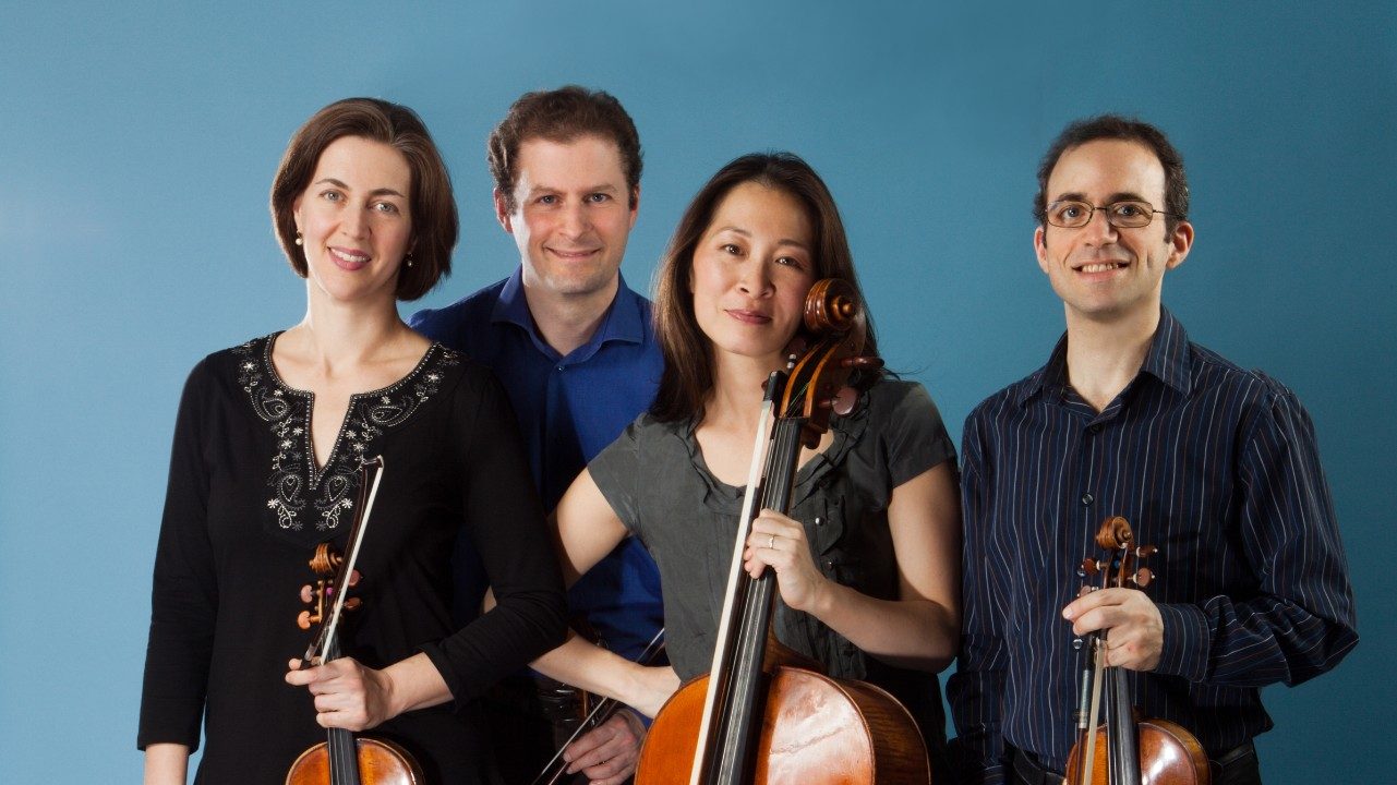  The Brentano String Quartet wears casual clothes and holds their instruments against a teal background. From left, a white woman, a white man, an Asian woman, and a white man.
