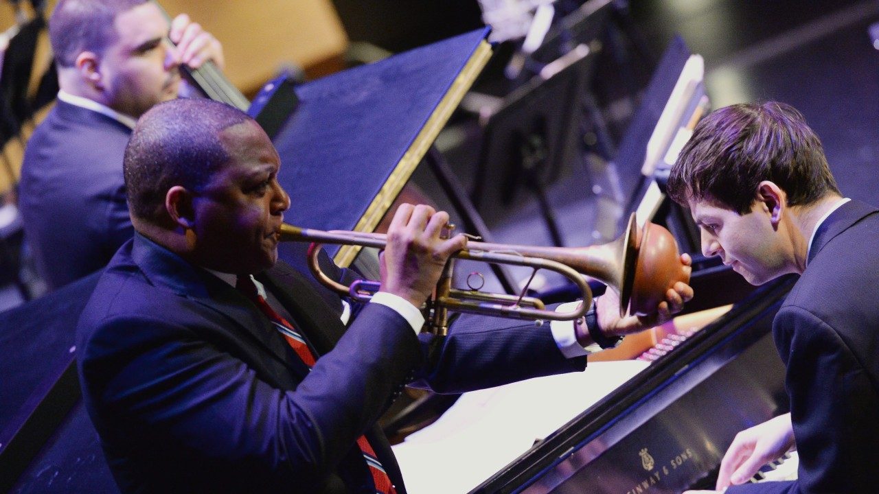 Wynton Marsalis plays his trumpet in the foreground, while other members of the Jazz at Lincoln Center Orchestra perform in the background.