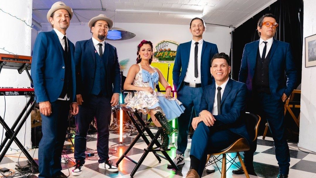  Members of East Los Angeles Chicano indie-folk band Las Cafeteras, five brown men in navy blue suits, and one brown woman (in the middle) in a rockabilly-inspired A-line floral halter dress and black combat boots.