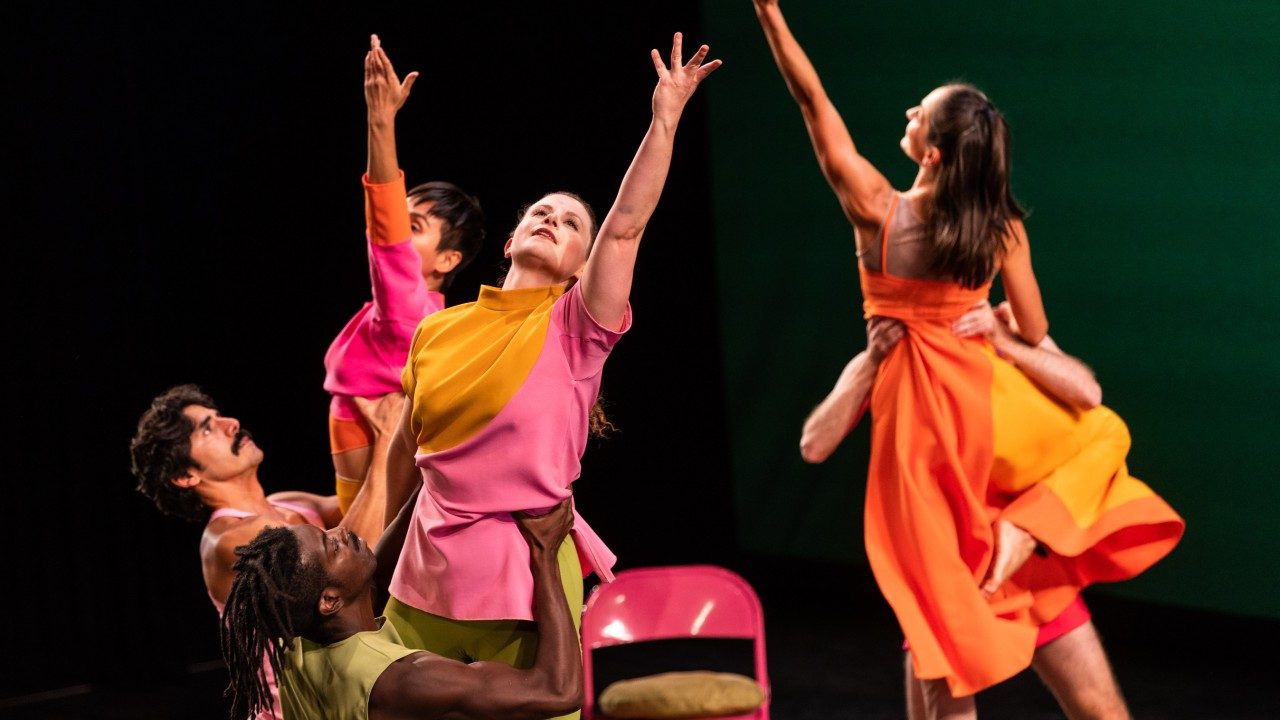  Dancers of Mark Morris Dance Group perform "The Look of Love" in bright, colorblocked uniforms. Three men lift three women in front of a dark green background.