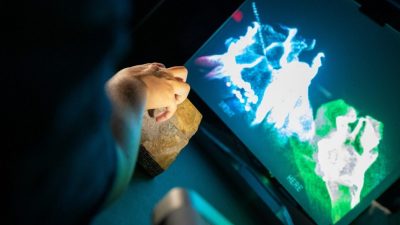 A hand touches a rock object in front of a projected screen as part of "Carving Out Creativity," one of three projects on view as part of this year's ICAT exhibition, "Open (at the) Source."