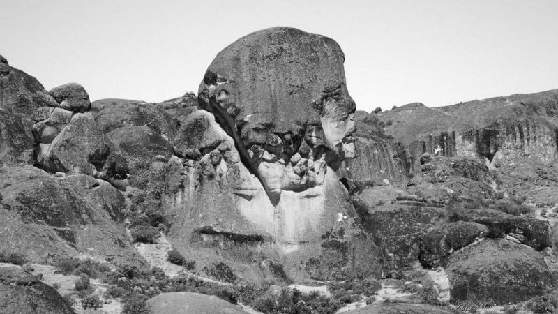 A black and white landscape image of a rock face in sweeping rocky hills.