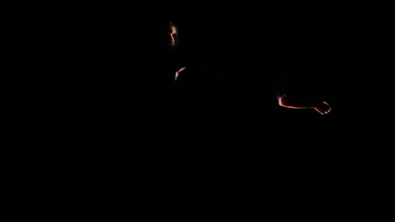 A person's arm and part of their face is illuminated in darkness, the rest of their body in shadow.