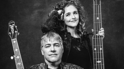 Banjoists Béla Fleck and Abigail Washburn  each hold the neck of banjos of widely varying sizes (Abigail's is taller than she is). She rests her elbow on the top of his head in this black and white image.
