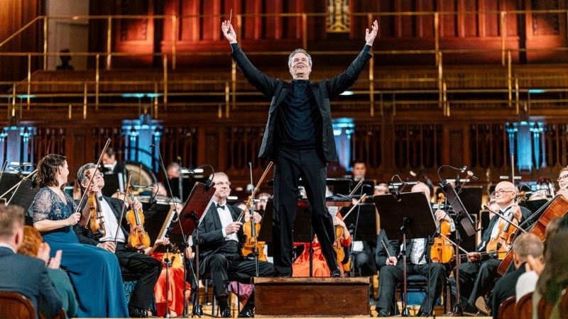 Conductor Steven Mercurio accepts applause from the audience, members of the Czech Symphony Orchestra surround him wearing concert attire.