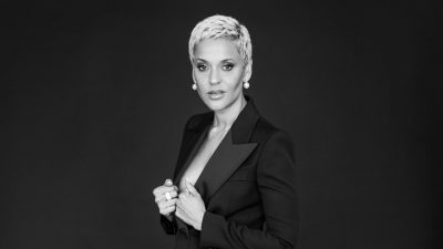 Fado singer Mariza, a Portuguese woman with short bleached blonde hair, wearing a black suit jacket against a dark background in this black and white image.