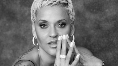 Fado singer Mariza, a Portuguese woman with short bleached blonde hair and tattoos, gazes towards the camera in this black and white image.