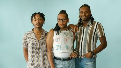 The members of the Harlem Gospel Travelers, three young Black singers wearing casual clothes in front of a pale blue background.