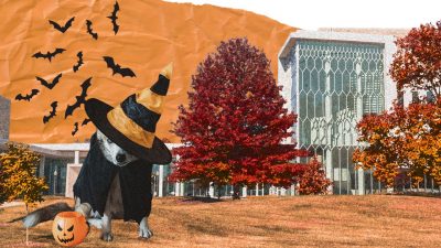The Center for the Arts at Virginia Tech in fall, with trees in reds and oranges. In front is a dog in a Halloween costume sitting next to a pumpkin trick or treat bucket. A group of bats flies in the air behind the dog.