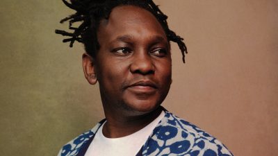 South African cellist Abel Selaocoe, a middle aged Black man with braids pulled up into a bun on the top of his head.