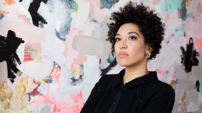 Soprano Julia Bullock stands in front of a brightly colored background of pinks, whites, blues, and blacks.