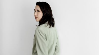 Conductor Miho Hazama, a young Asian woman, wears and oversized beige blazer in front of a light grey background.