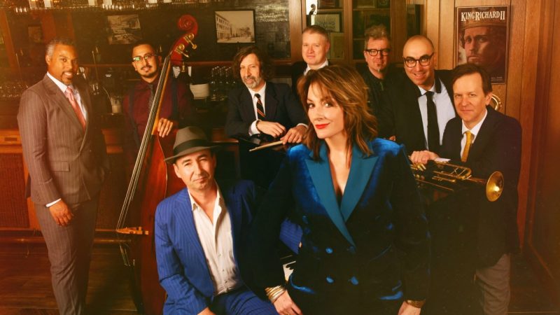 The members of New York jazz ensemble the Hot Sardines gathers in a jazz club, some holding their instruments.