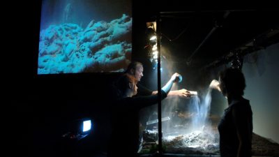 Members of Hotel Modern perform "The Great War," scattering sand down on a miniature set to mimic snow during wartime.