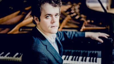 Pianist Benjamin Grosvener, a white man with brown hair and blue eyes, sits at his piano.