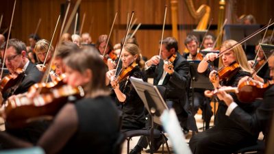 Members of the string section of the Royal Philharmonic Orchestra perform on stage in concert.