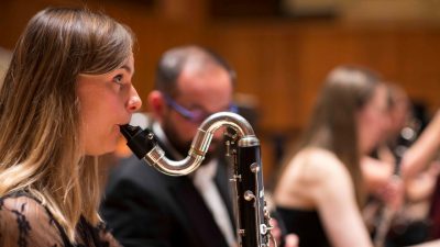 A member of the Royal Philharmonic Orchestra plays a wind instrument on stage during a concert.