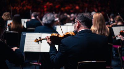 A member of the Royal Philharmonic Orchestra plays a violin on stage during a concert.
