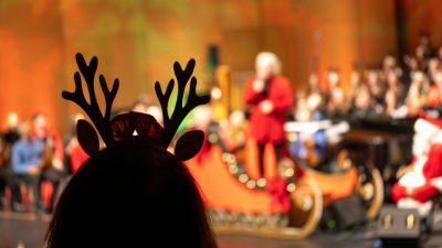 A woman wearing reindeer antlers watches the Roanoke Symphony Orchestra's "Holiday Pops Spectacular" as conductor David Stewart Wiley speaks and Santa looks on.