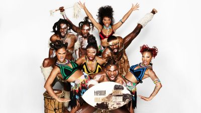 Members of Step Afrika! pose as a group in traditional African garments in a studio.
