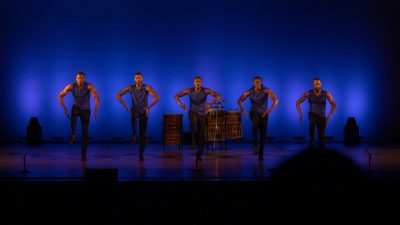 Members of Step Afrika! perform in a row on stage.