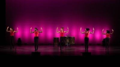 Female members of Step Afrika! perform in a row on stage.