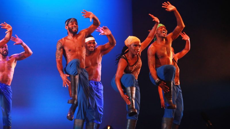 Members of Step Afrika! perform in blue pants and black rain boots on stage.