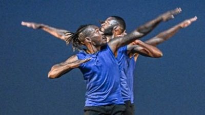 Male members of Step Afrika! in blue costumes perform on stage.
