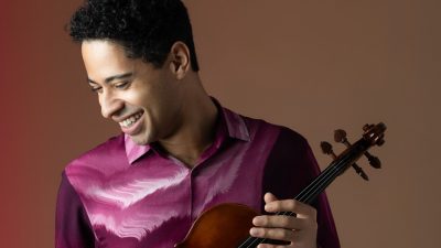 Violist Jordan Bak wears a maroon patterned button down shirt and holds his instrument.