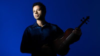 Violist Jordan Bak wears a navy blue button down shirt and holds his instrument.