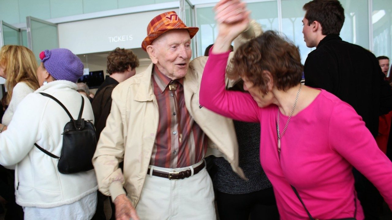  Older gentleman in a VT hat dancing with a woman in the grand lobby which is full of people