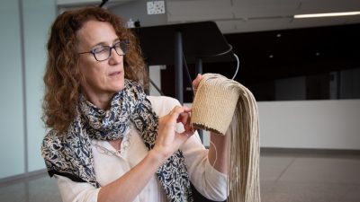  An artist, a white woman with curly shoulder length red hair and black rimmed glasses, leads a basketweaving demonstration in the Moss Arts Center Grand Lobby.